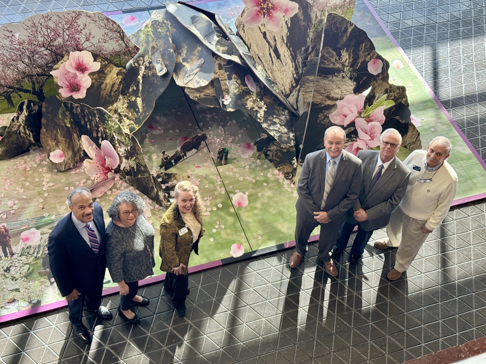 Six people standing in front of a large art display on the floor and looking up