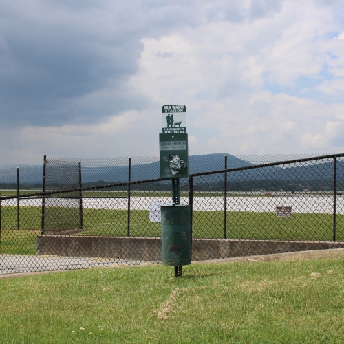A grassy area with chain link fencing and a dog waste station sign