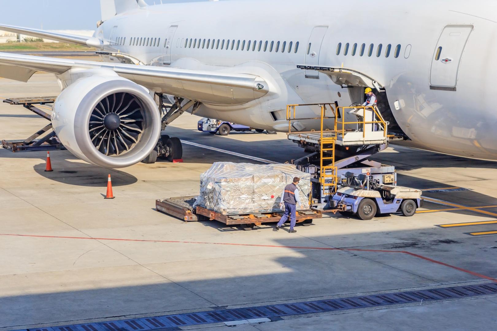 A large plane sitting on a tarmac with a pallet of cargo being loaded onto it