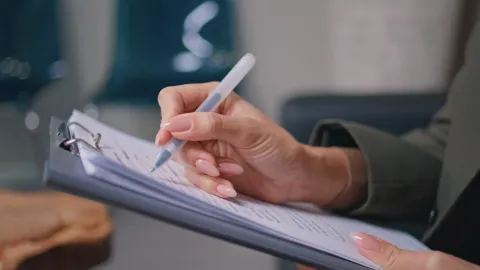 A closeup of a person holding an ink pen filling out a form on a clipboard